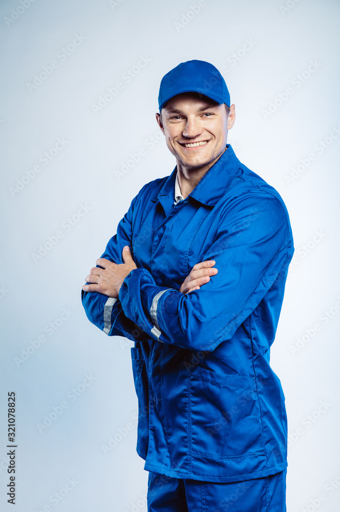 Portrait of young worker man wearing blue uniform with crossing hands. Isolated on grey background with copy space. Human face expression, emotion. Business concept.