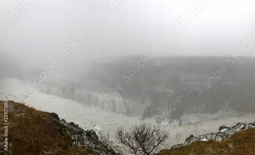 Breathtaking scenery at the Gullfoss Golden Waterfall landmark, a nature attraction in Iceland: Arctic nature with majestic rocks, the Hvita river running in the winter canyon with a cloudy white sky