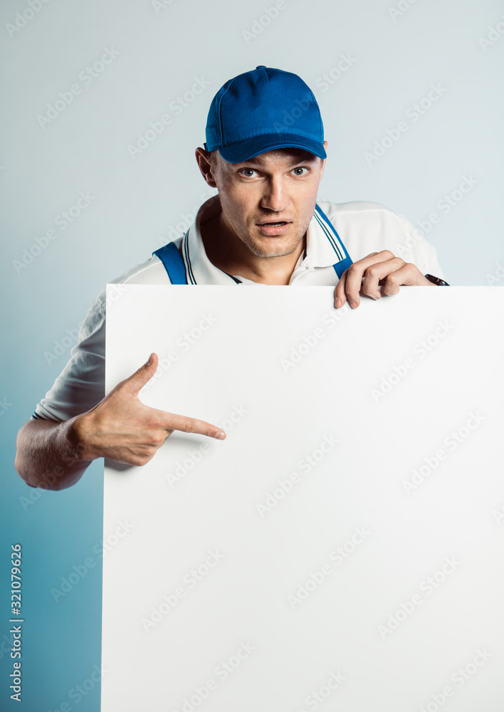 Mockup image of a young worker holding empty white banner and points to it. Mockup image of a young worker holding empty white banner and points to it.