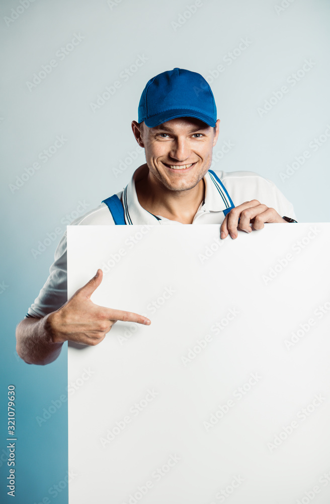 Mockup image of a young smiling worker holding empty white banner and points to it. Mockup image of a young smiling worker holding empty white banner and points to it.