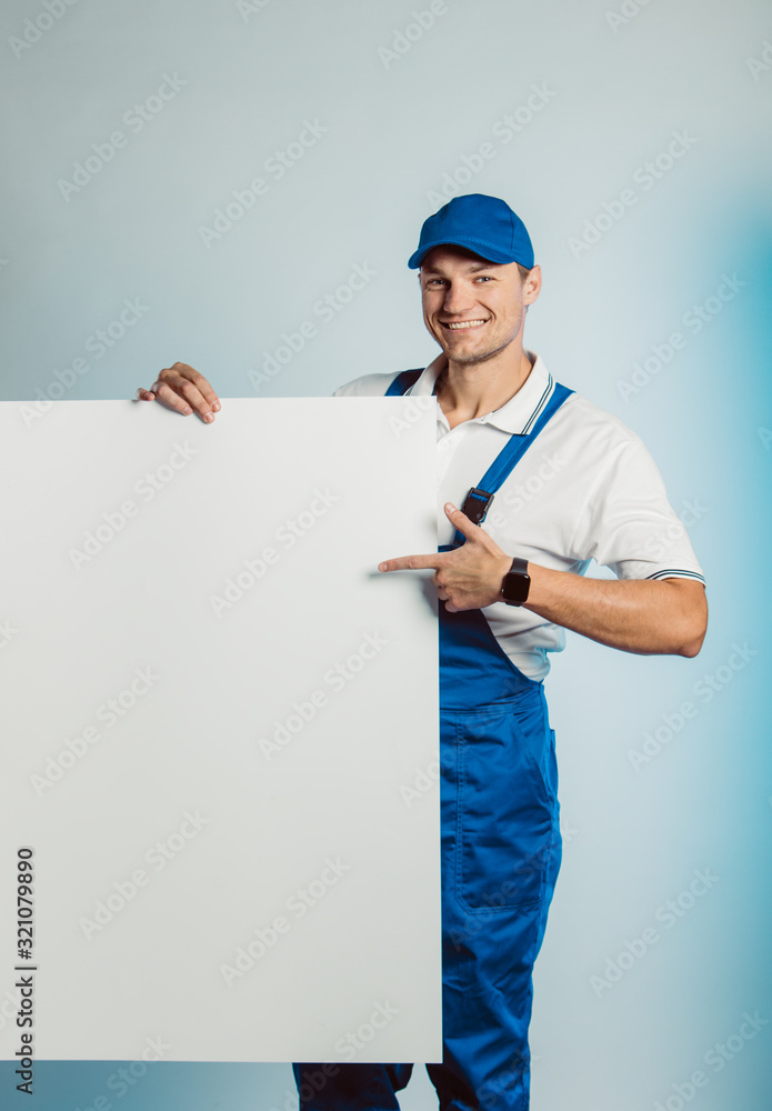 Mockup image of a young smiling worker holding empty white banner and points to it. Mockup image of a young smiling worker holding empty white banner and points to it.