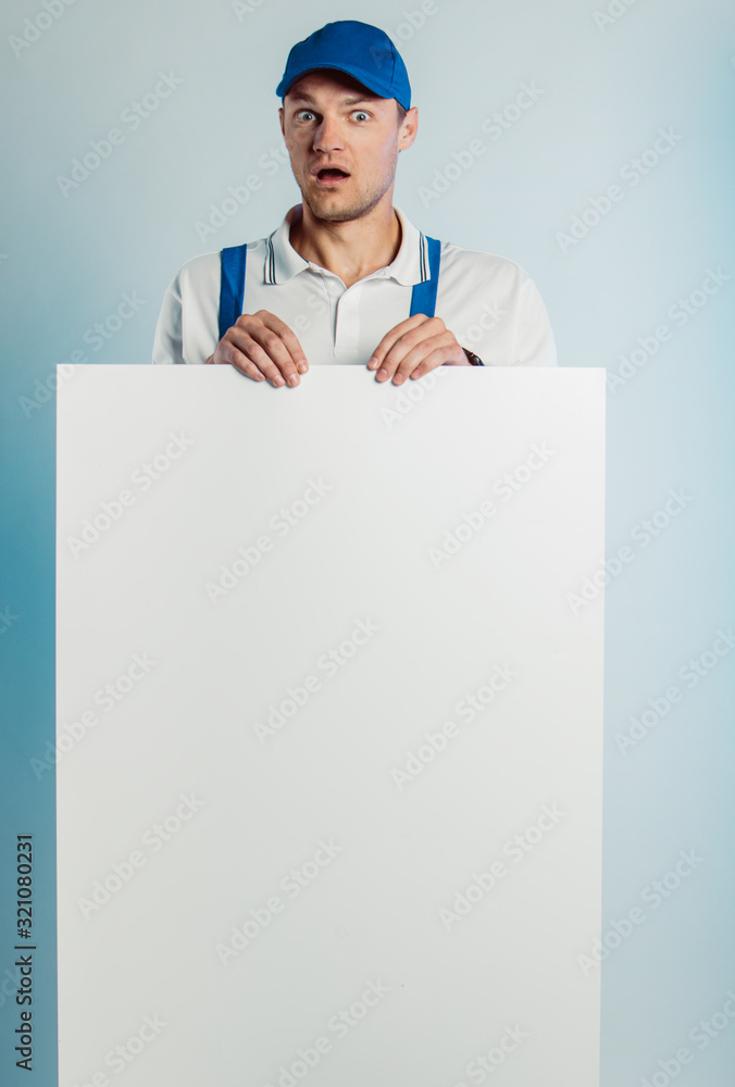 Mockup image of a young surprised worker holding empty white banner. White or blue background. Bussines concept. Mockup image of a young surprised worker holding empty white banner. White or blue background. Bussines concept.