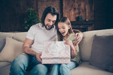 Photo of little adorable funny lady and her handsome young daddy sit cozy sofa giving receiving large giftbox birthday present gift celebrate domestic atmosphere indoors