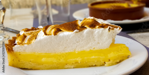 Fotografie Lemon meringue pie on a restaurant table with crème brûlée in the background