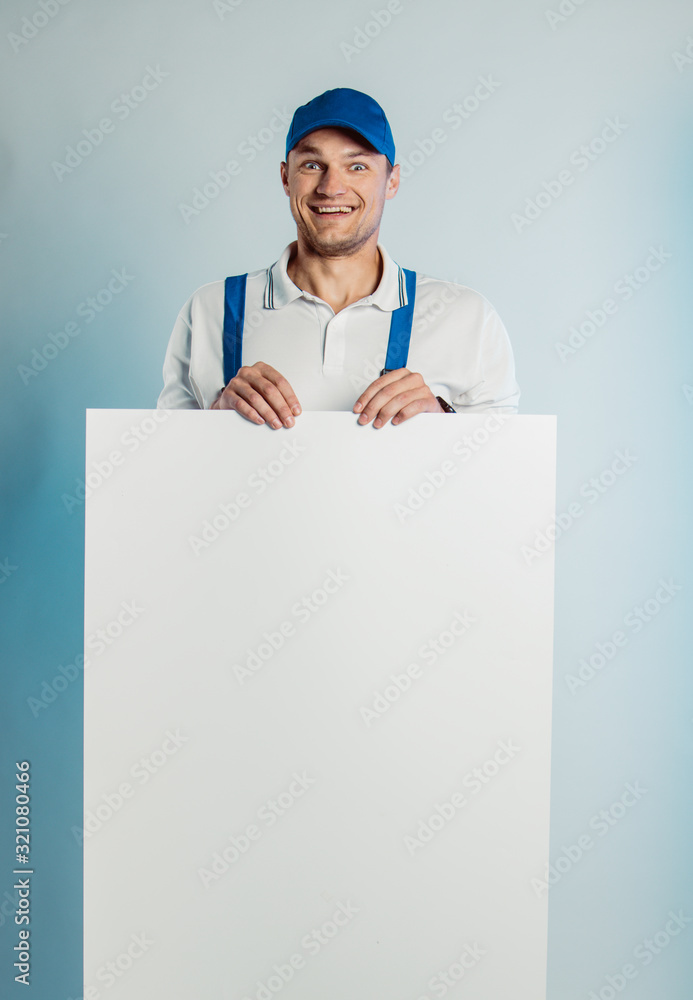 Mockup image of a young high smiling worker holding empty white banner. White or blue background. Bussines concept. Mockup image of a young high smiling worker holding empty white banner. White or blue background. Bussines concept.