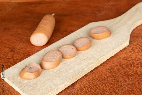 Group of five slices one piece of pork frankfurt sausage on wooden cutting board on cognac leather