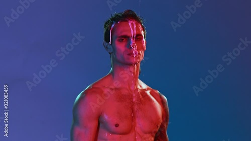 Vivid neon style photo session of young handsome gay man or freak stripper. Red and blue light on athletic built guy, isolated background, thick white liquid flowing over head and tattooed body photo