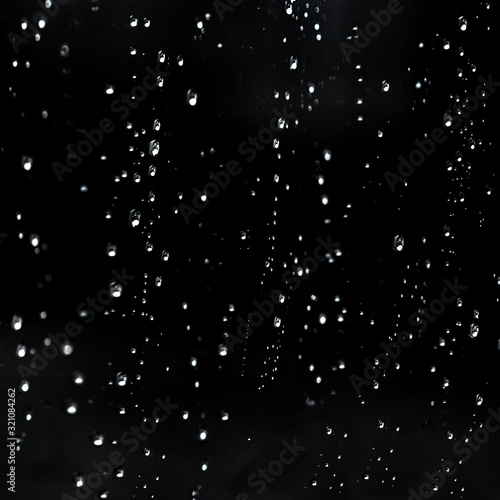 Falling Rain water drops on a black dramatic window glass. Autumn depression background. Rain pattern.
