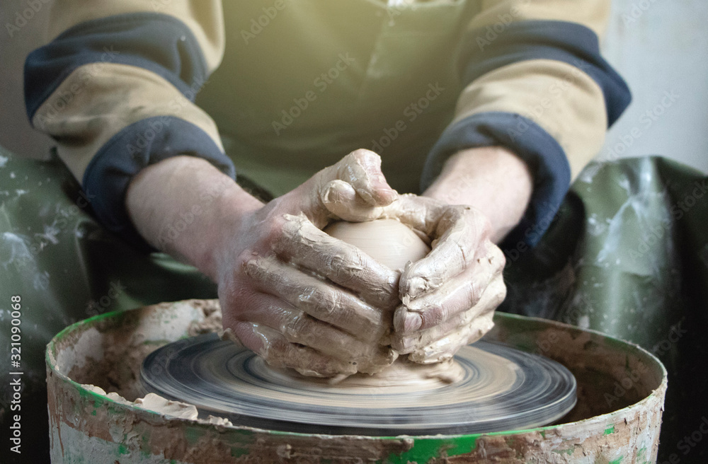 Hands of a potter on a pottery wheel close-up. Old traditional art, handmade, clay and ceramic production. Pottery workshop in subdued soft light
