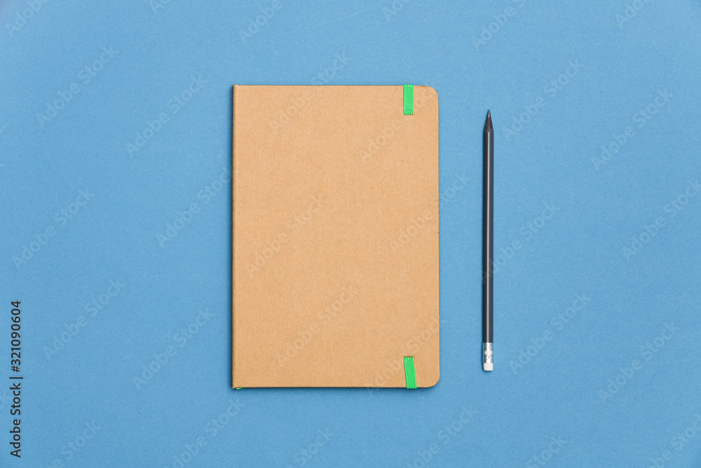 Top view of closed craft cover notebook with pencil on blue desk background. Top view of closed craft cover notebook with pencil on blue desk background.