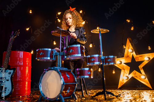 Beautiful girl with curly hair playing the drums on a black illuminated background