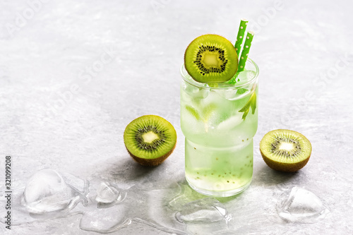 A refreshing summer drink with slices of kiwi and ice in a glass on a gray background. Selective focus.