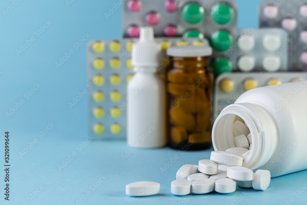 Pills spilling out of white bottle on blue background. with copy space. Pharmaceutical medicament, cure in container for health. Medicine concept Pills spilling out of white bottle on blue background. with copy space. Pharmaceutical medicament, cure in container for health. Medicine concept