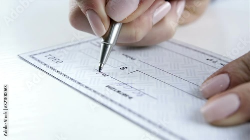 Female hand with pen filling a bank check. Paycheck concept. Payment by cheque