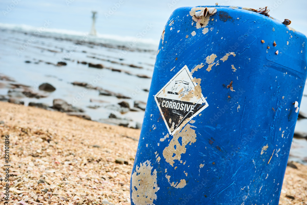 Naklejka premium Blue canister laying on a beach in japan with a chemical corosive sign on it demonstrating ocean pollution and environment pollution