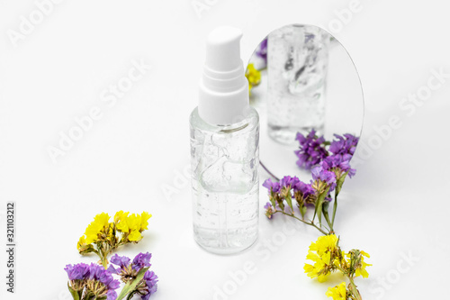 Cosmetic bottle with serum, gel, face cream on a white background with flowers. Skin cosmetics, minimalism