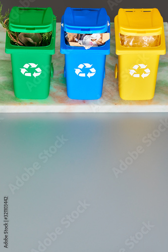 Three color coded recycle bins, isometric projection on grey background with copy-space. Recycling sign on the bins, blue, yellow and green. Waste separation to reduce antropogenic pressure. photo