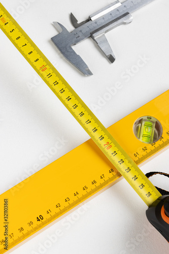 Yellow tape measure, spirit level,and caliper on clear white background. Vertical photo. Place for text.
