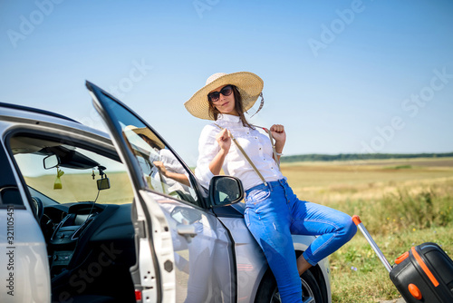young happy beautiful model near her car on summer trip.