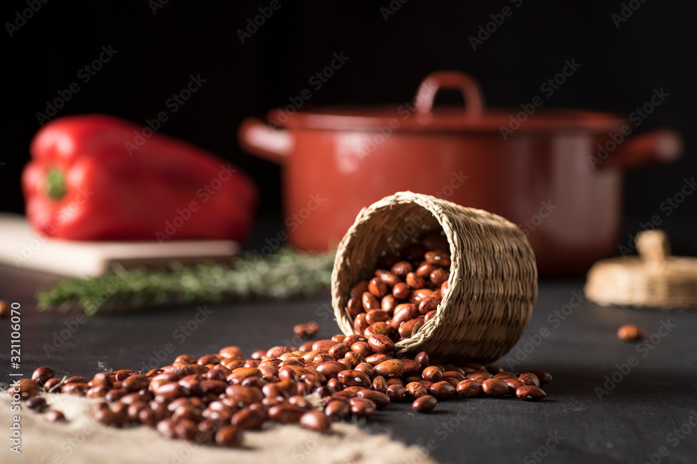table with black beans in a wicker bowl and on a piece of esparto, next to a casserole and a red pepper