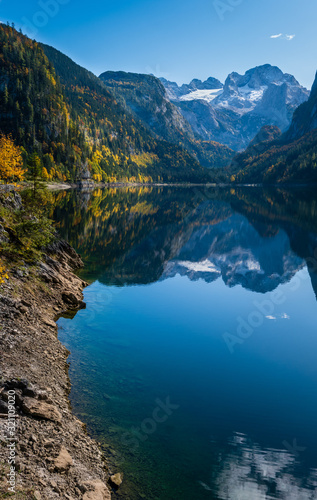 Fototapeta Naklejka Na Ścianę i Meble -  Peaceful autumn Alps mountain lake with clear transparent water and reflections. Gosauseen or Vorderer Gosausee lake, Upper Austria. Dachstein summit and glacier in far.