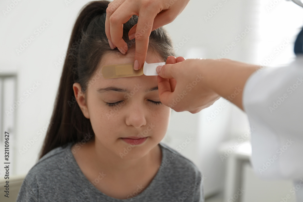 Naklejka premium Doctor putting sticking plaster onto girl's forehead indoors