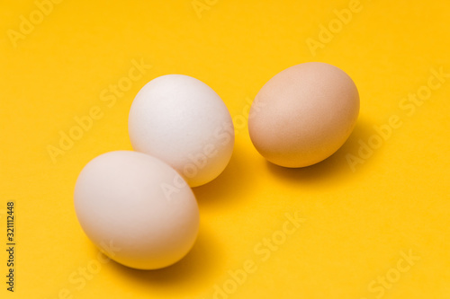 closeup of three natural color ecological eggs on yellow background randomly alined