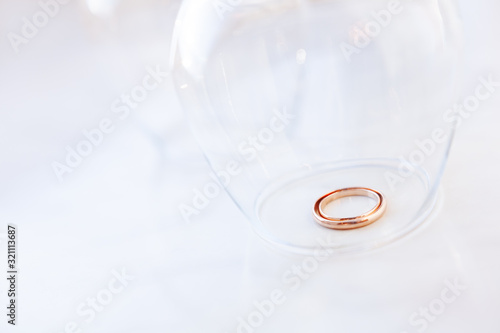 Golden wedding rings under transparent wine glass. Symbol of love and marriage.