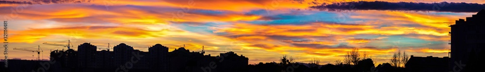 Panorama of colorful sunset sky over the silhouettes of houses