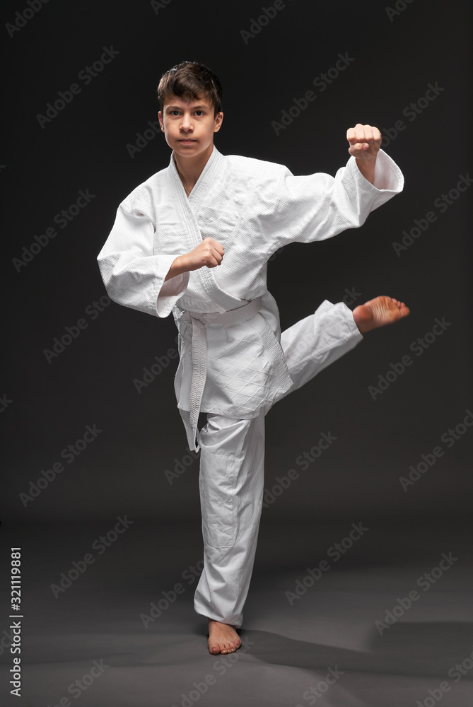 a teenager dressed in martial arts clothing poses on a dark gray background, a sports concept