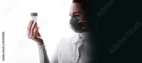 Portrait of young female researcher with test tube in hand. Serious woman in protective medical mask, respirator. Free space for text. White background. Healthcare concept.
