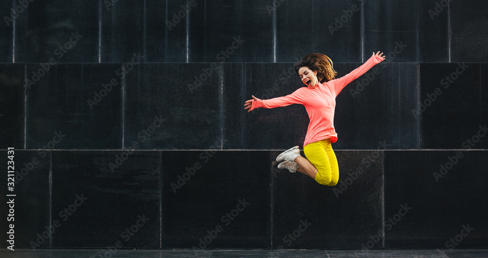 Beautiful fit smiling young woman jumping in air with raised hands