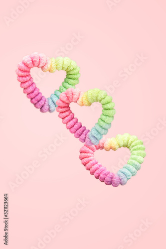 Creative valentine's abstract design layout with hearts made from retro rainbow crunchie balancing in the air isoalted on pink background. Beauty and fashion concept photo