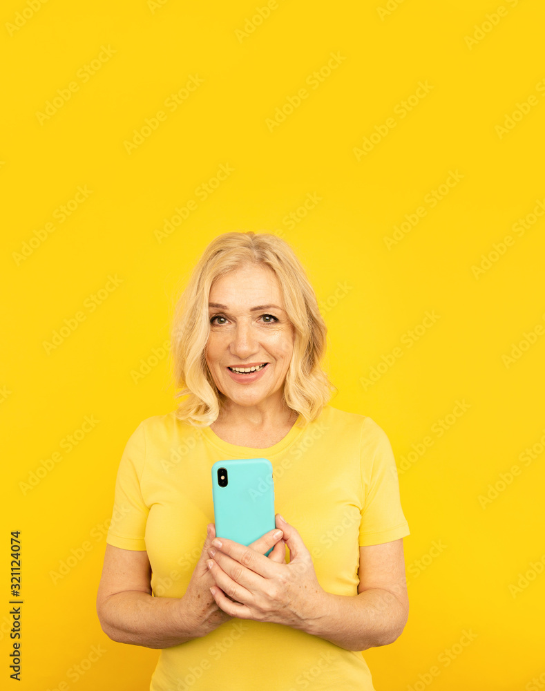 Happy adult female with blue mobile on the yellow background Happy adult female with blue mobile on the yellow background