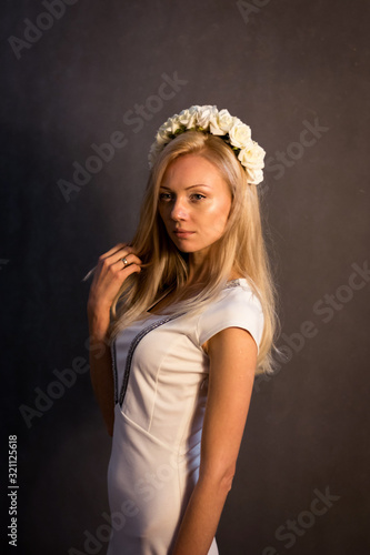 Beautiful blonde girl in the studio. In a white dress, on a dark background.