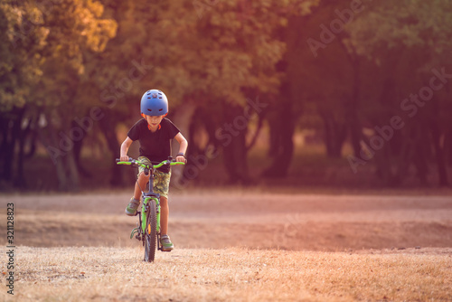 Fototapeta Naklejka Na Ścianę i Meble -  Happy kid boy of 7 years having fun in autumn park with a bicycle on beautiful fall day. Active child wearing bike helmet