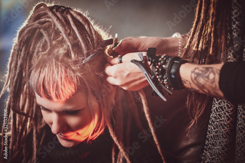 Pretty young woman is receiving new hairstyle from dreadlocks master.