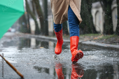 Foto Woman in rubber boots running after umbrella outdoors on rainy day, closeup