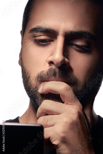 Bearded Arab guy using smartphone and thinking with his hand on mouth isolated on white