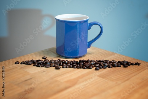 Blue cup of black coffee with coffee beans on a wooden table surface