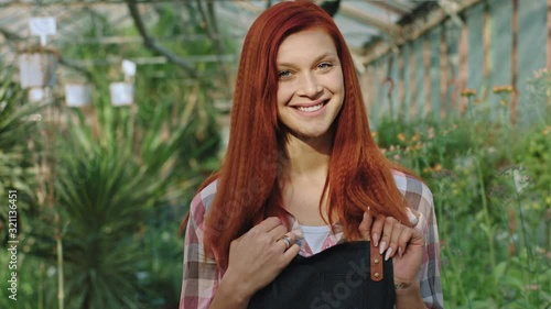 Amazing looking gardener woman with a large smile looking in front of the camera posing happy background large flower greenhouse