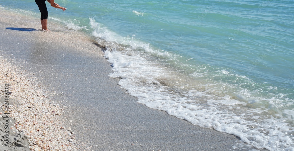 Stooping to collect shells on the beach by the sea in Sanibel Island, Florida Stooping to collect shells on the beach by the sea in Sanibel Island, Florida