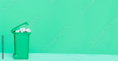 A green plastic garbage bin and paper on green background, great for recycling concepts and designs.
