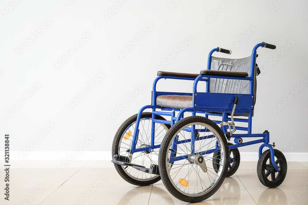 Fototapeta premium Empty wheelchair near light wall