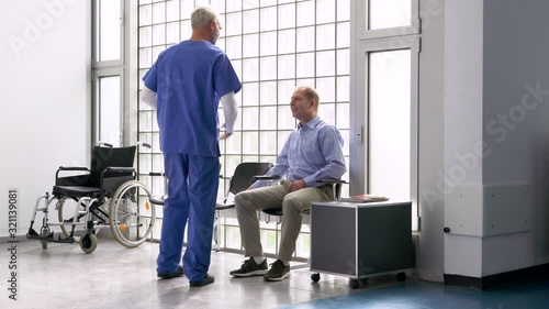 Handheld shot of male doctor greeting and talking with patient in hospital waiting room