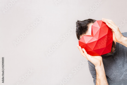 Fotografie Man holding polygonal diamond shaped red heart in front of his face
