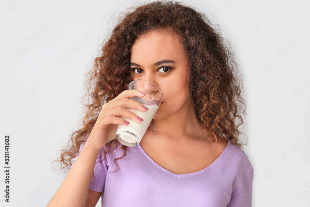 Young African-American woman with milk on grey background Young African-American woman with milk on grey background