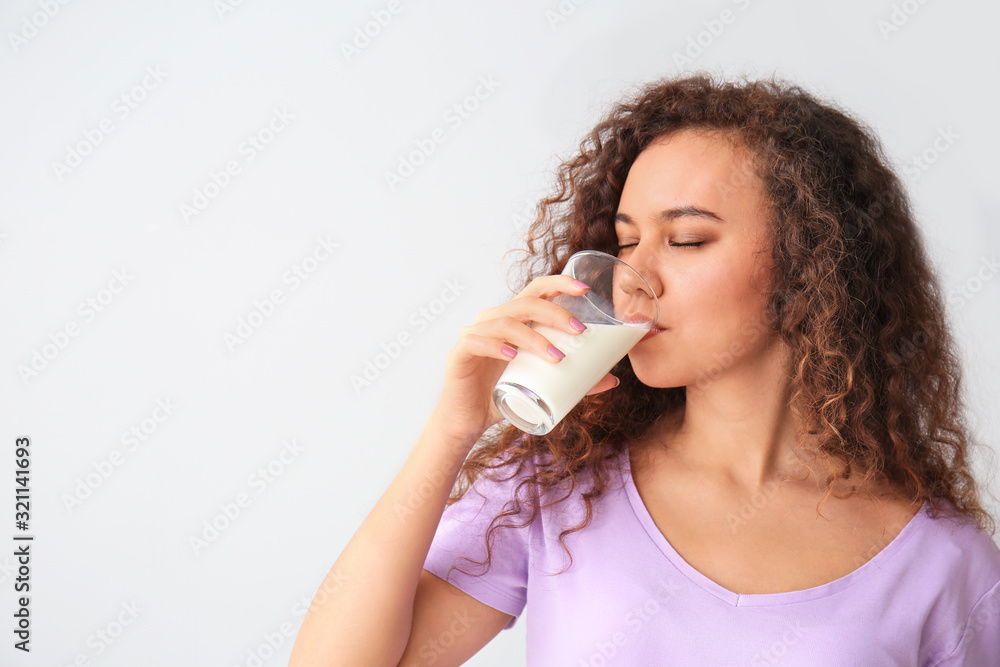 Young African-American woman with milk on grey background Young African-American woman with milk on grey background