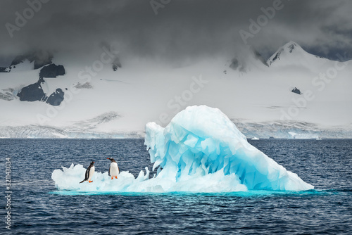 two penguins float on the blue iceberg in ocean