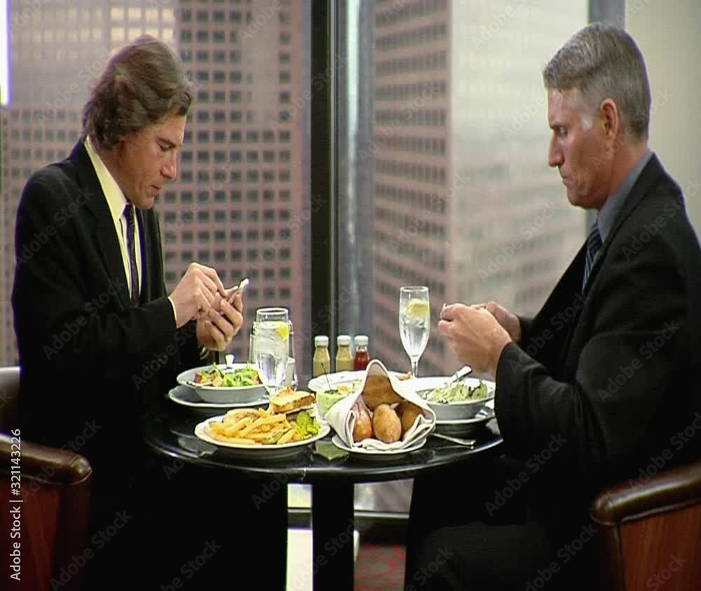 MS, Lockdown, Two businessmen having a business lunch while both using their mobile phones MS, Lockdown, Two businessmen having a business lunch while both using their mobile phones